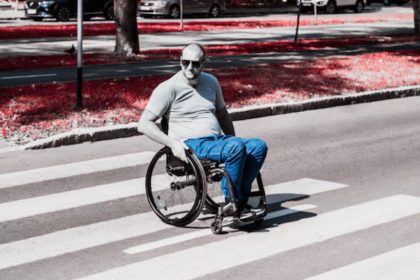 Hombre en silla de ruedas cruza una calle usando una rampa de banqueta en una zona urbana.